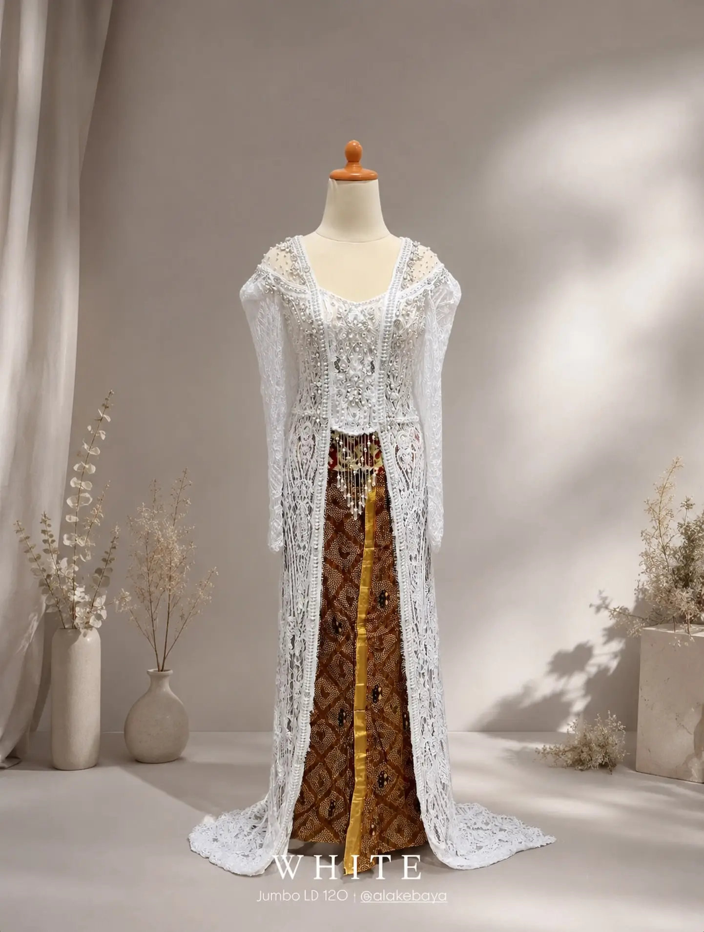 Kebaya brokat putih dengan kain batik cokelat pada manekin, koleksi sewa @alakebaya