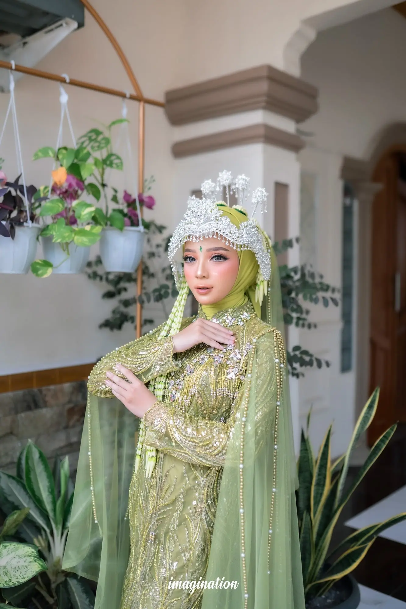 Pengantin bergaun hijau sage dengan siger putih berpose di teras rumah