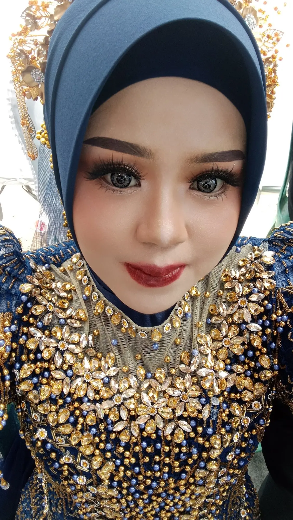 Makeup pesta dengan hijab biru dan busana biru tua berpayet emas