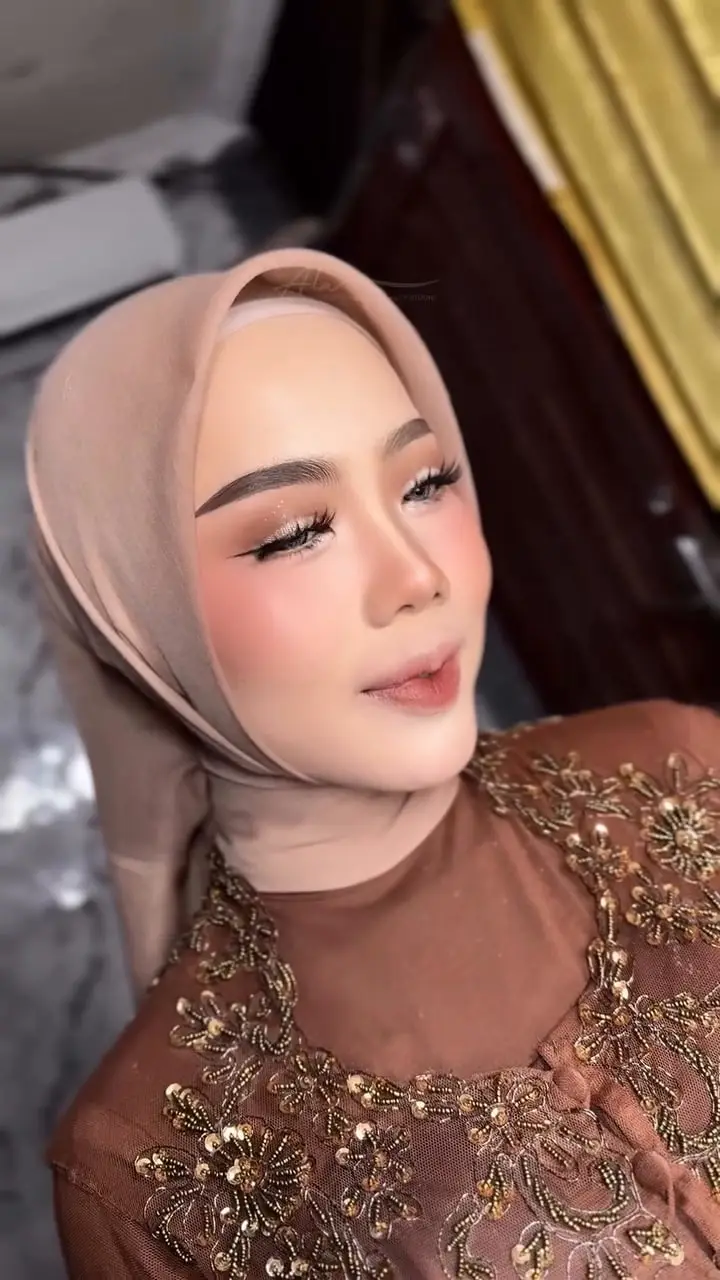 Makeup lamaran Liddya berhijab krem dengan kebaya cokelat berpayet emas