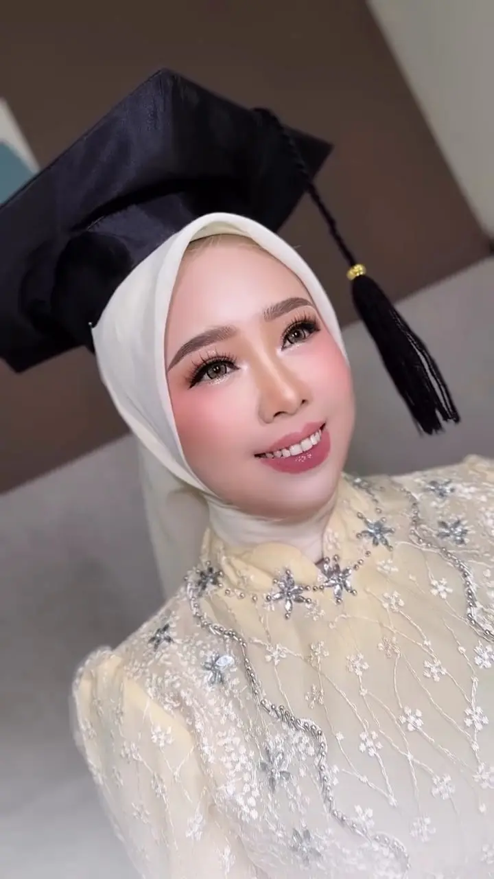 Makeup wisuda Okeu berhijab putih dengan toga dan kebaya krem
