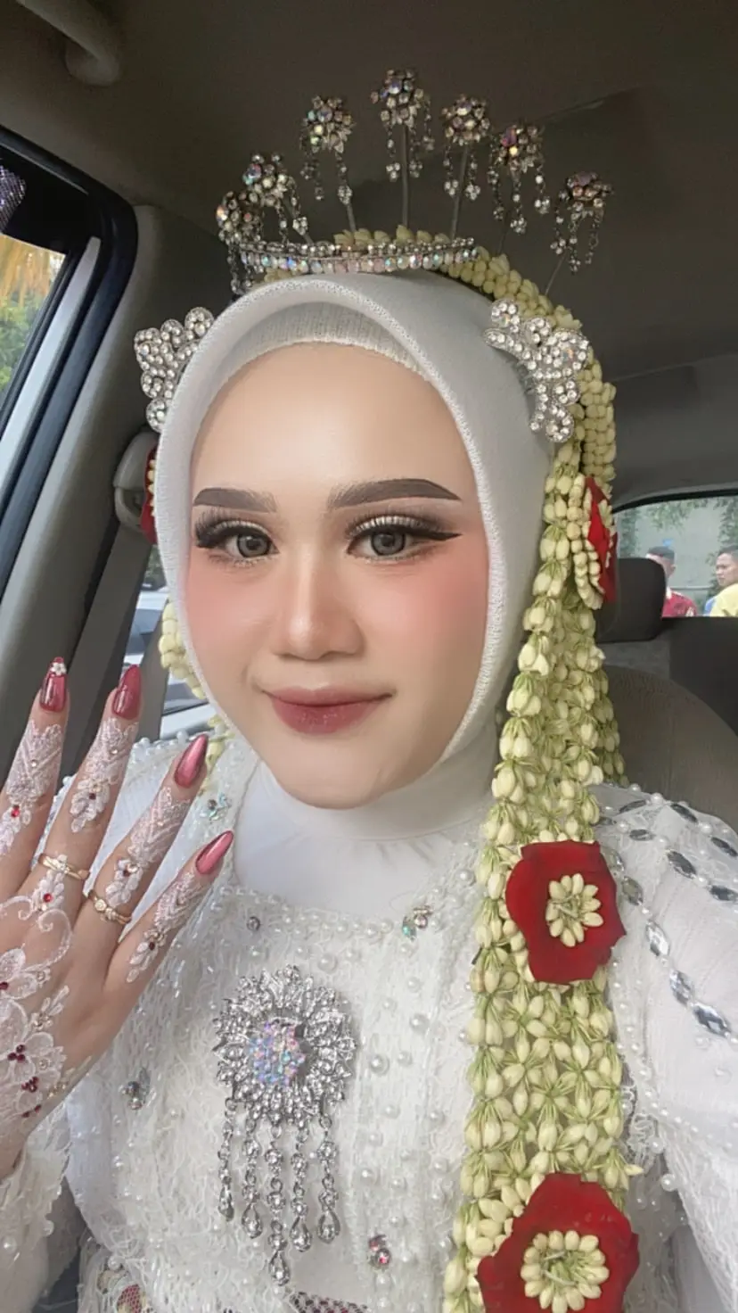 Pengantin berhijab putih dengan siger, ronce melati, dan kuku berhias, berfoto di dalam mobil