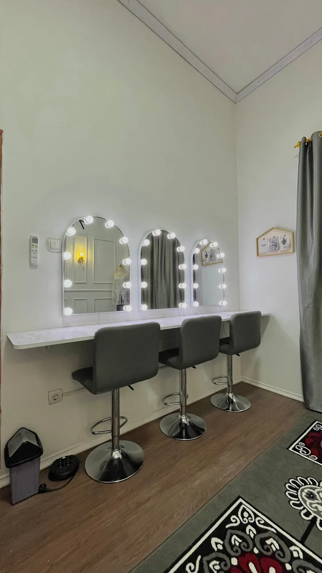 Meja rias studio dengan tiga cermin berlampu dan kursi tinggi