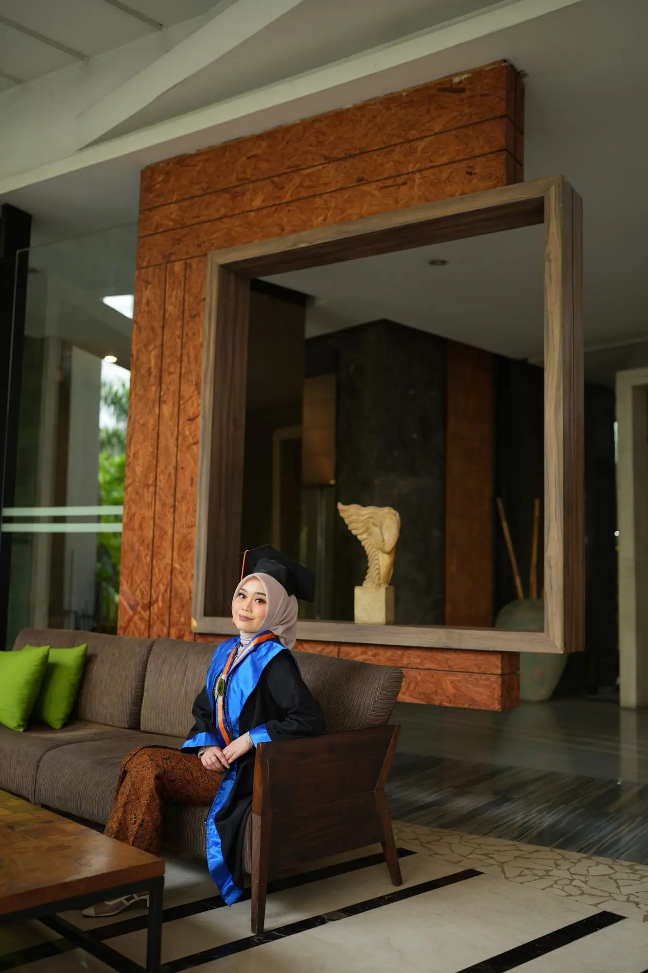 Wisudawati berhijab dengan toga duduk di lobi setelah dirias